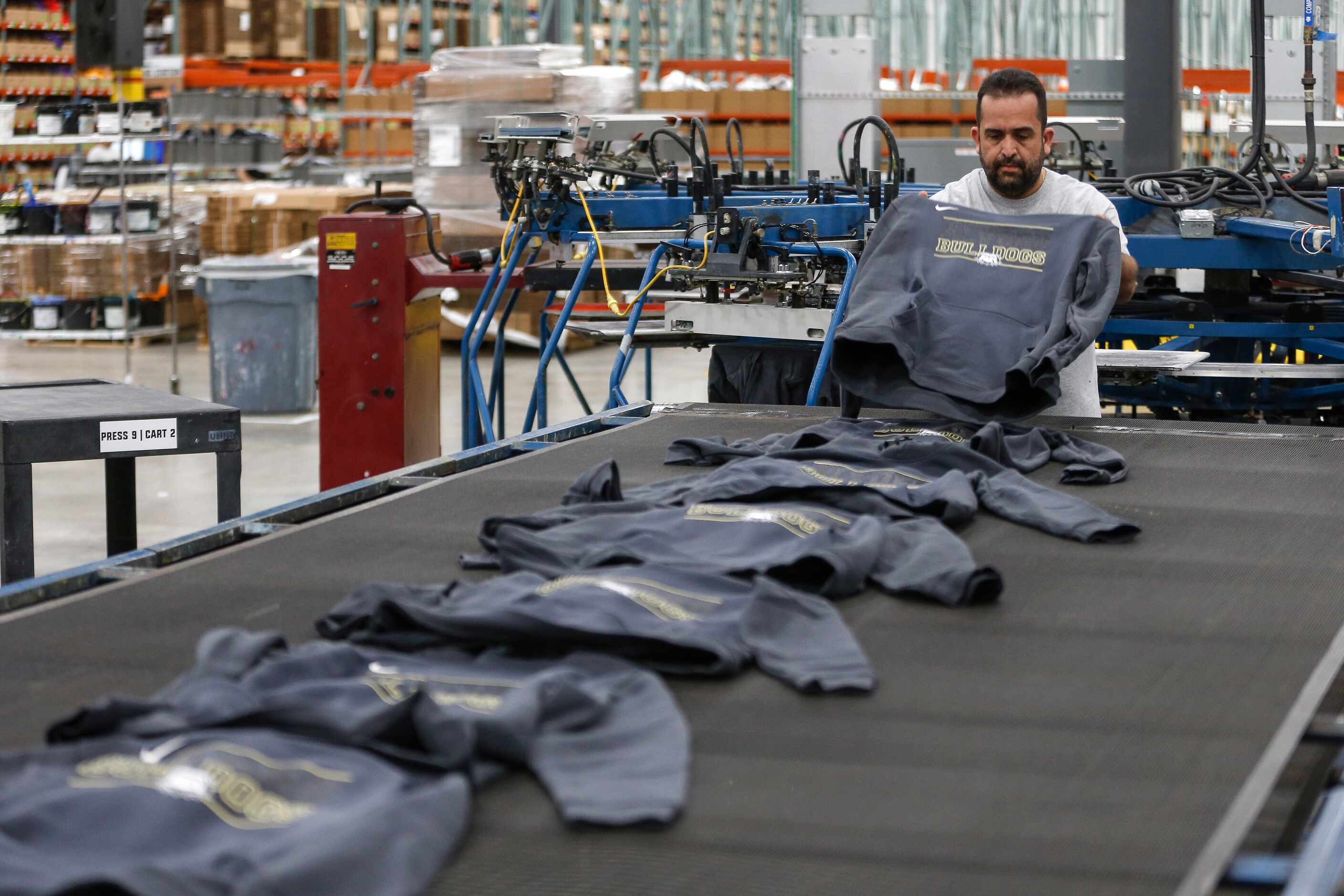 Workers work on custom design apparel orders at BSN Sports on Thursday.