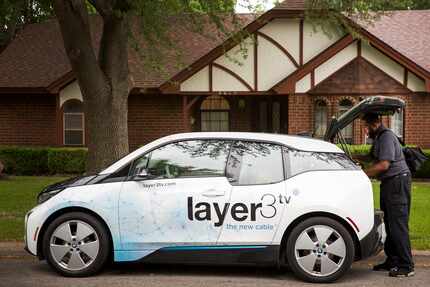 Keith Hamilton of Layer3 grabs gear from his car, a BMW i3, as he installs cable TV...