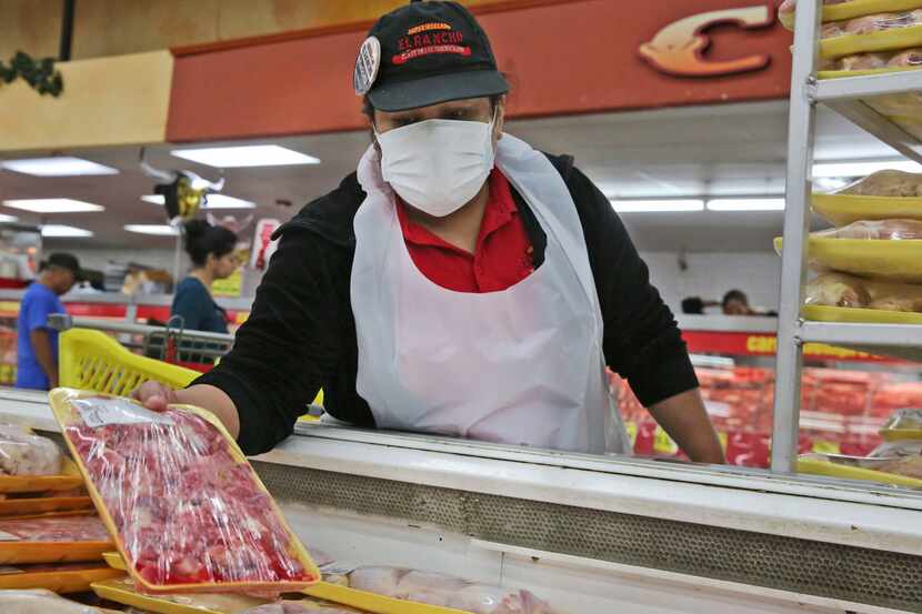 Marcela Martinez Salazar wears a mask while restocking at El Rancho grocery store in Dallas...