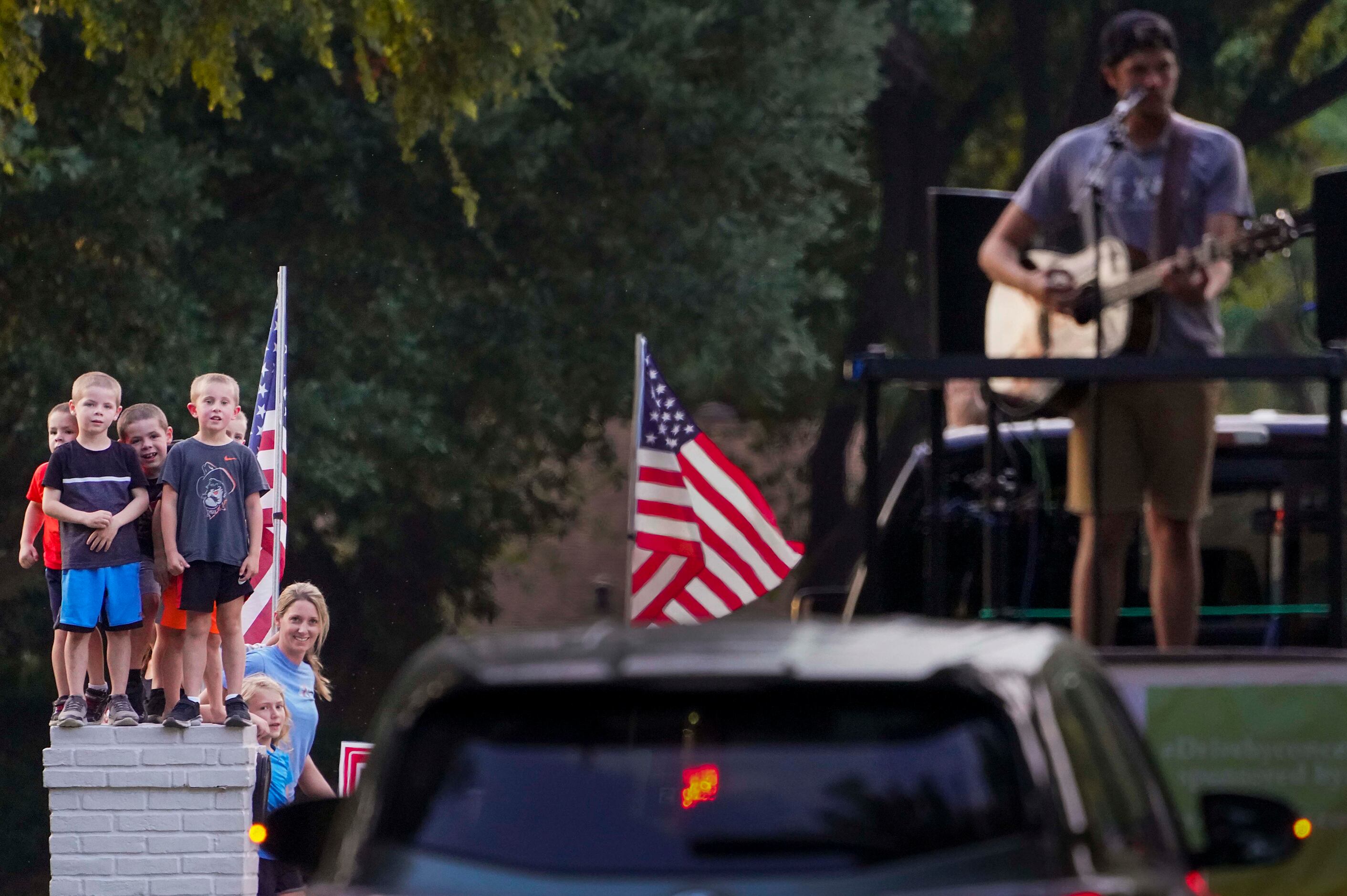 Neighborhood kids stand atop a mailbox as Cameron Havens sings from the back of a pickup...