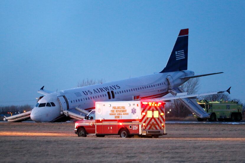 Emergency vehicles drive past a damaged US Airways jet at the end of a runway at ...