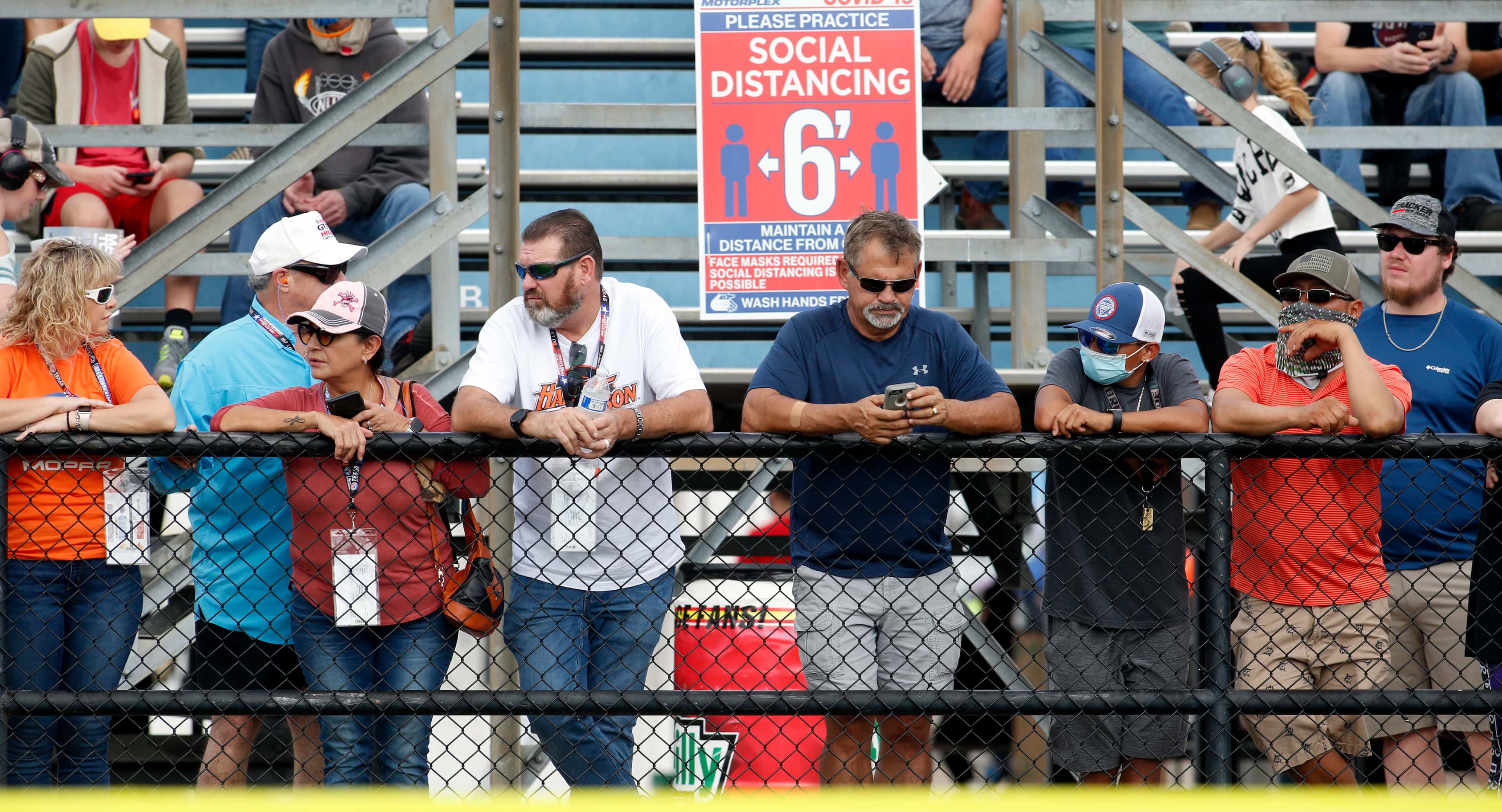 Racing enthusiasts stand along a rail as they await the start of a race in the funny car...
