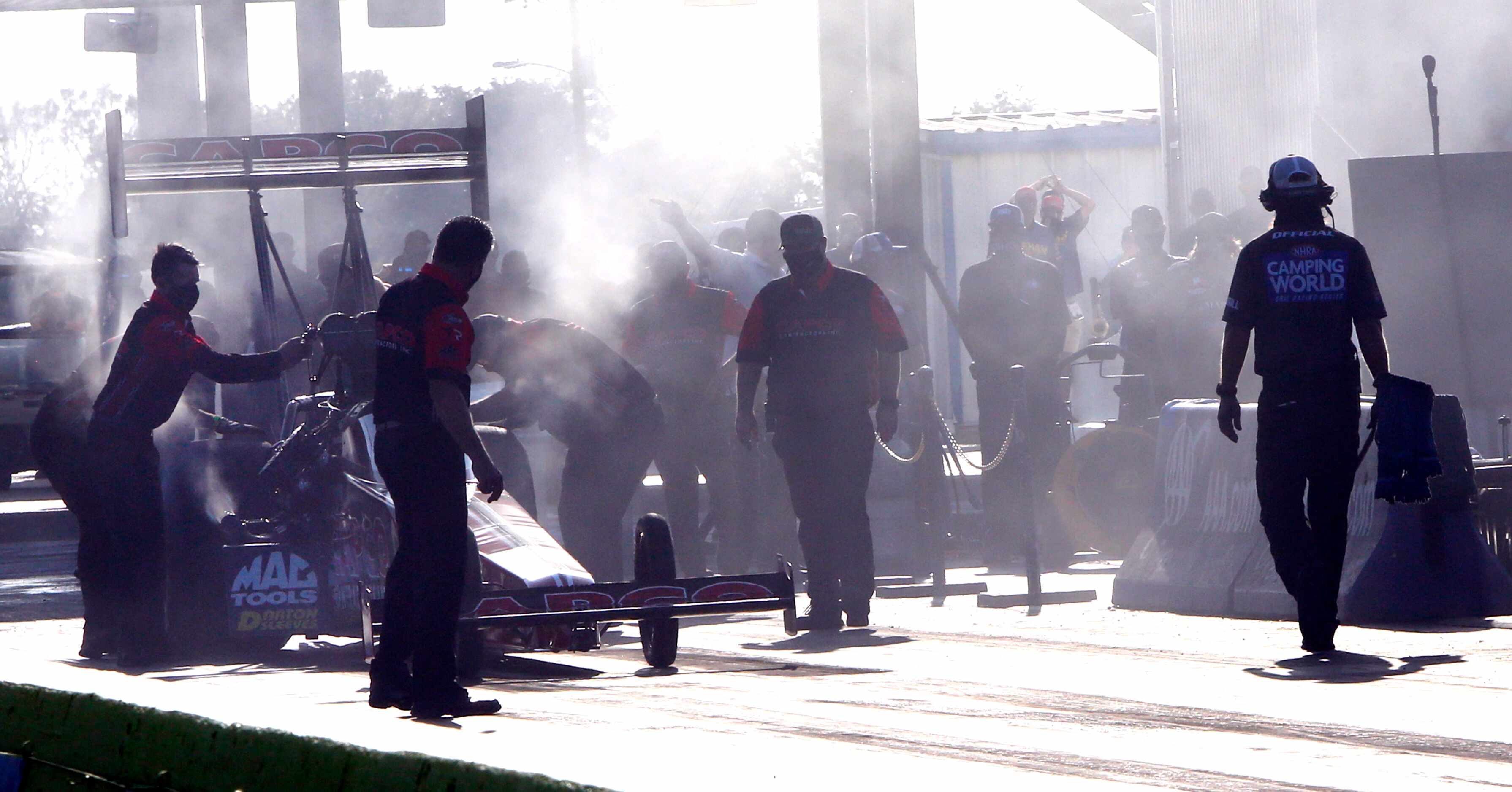 Pit crew members work to prepare a race car under smoky conditions at the starting line.The...