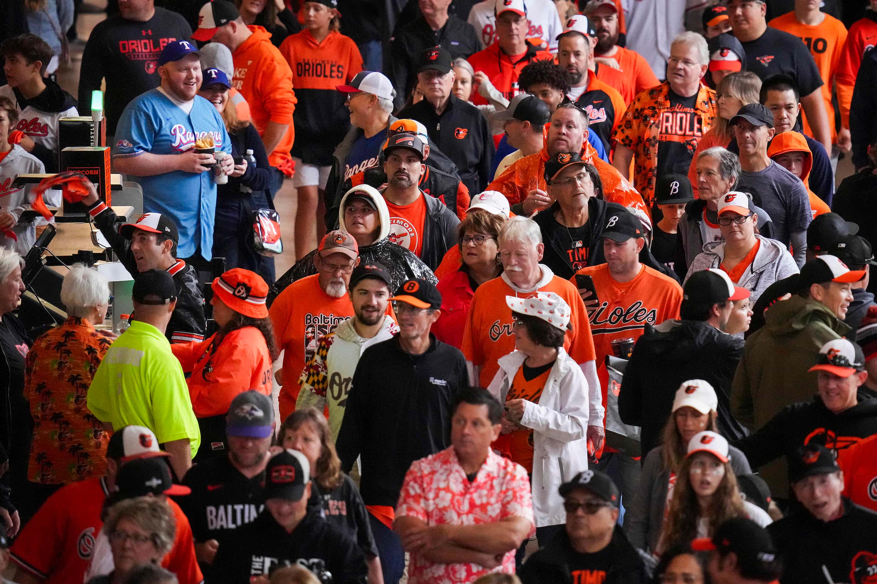 A pair of Texas Rangers fans looks out over a crowded concourse of Baltimore Orioles fans...
