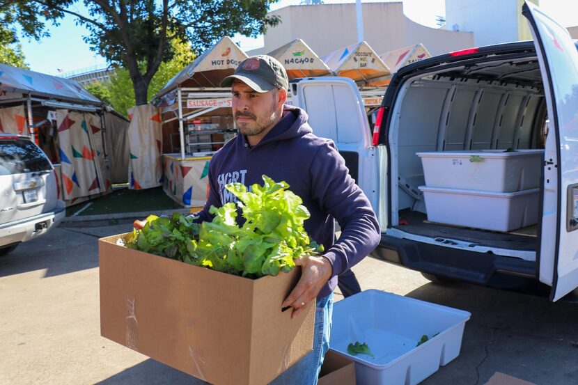 A man carries a box full of produce out of a van.