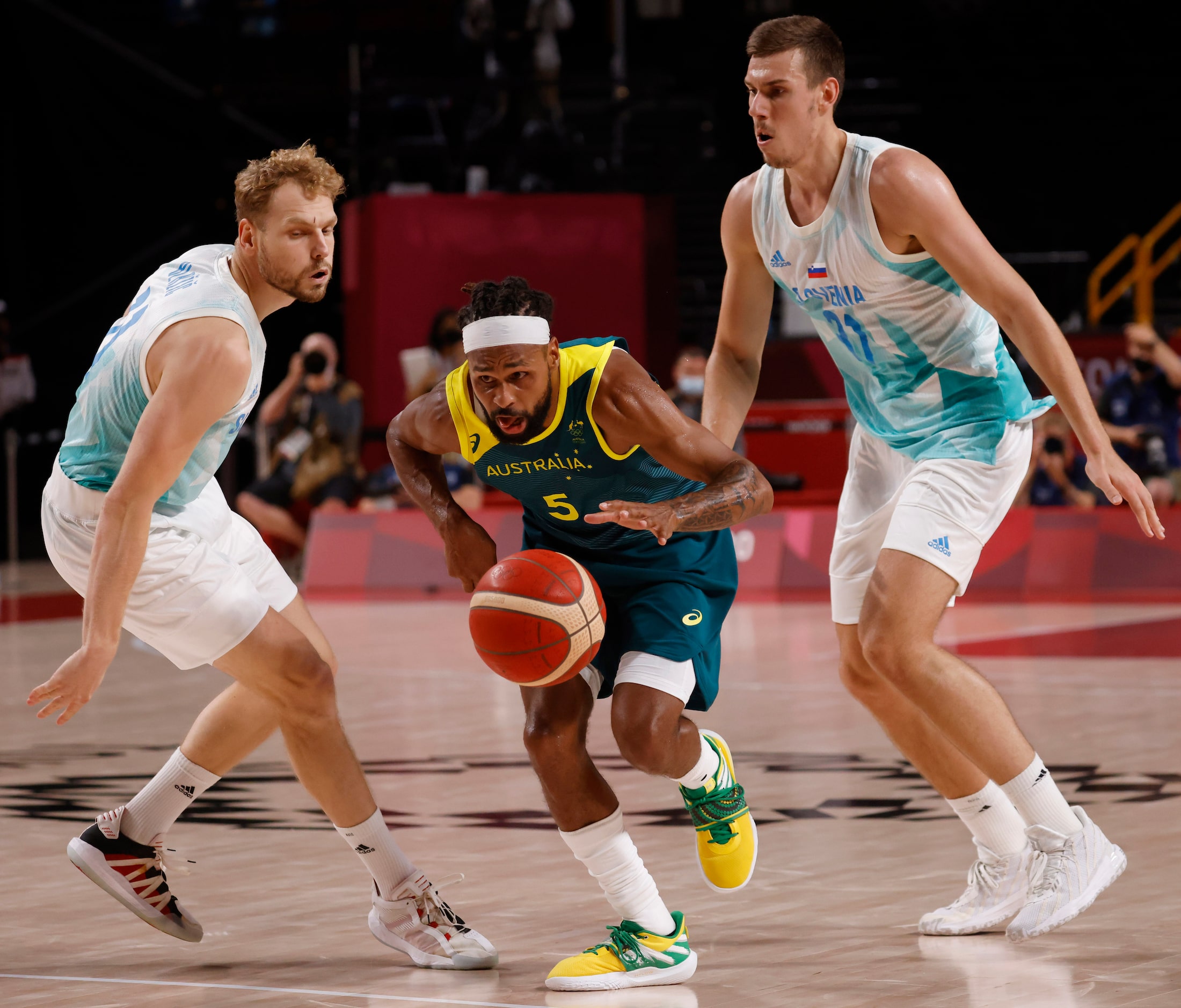 Australia’s Patty Mills (5) splits Slovenia defenders Jaka Blazic (11) and Vlatko Cancar...