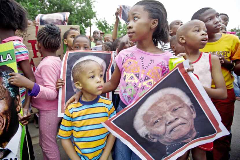 South African children, with placards of Nelson Mandela, celebrated his life Friday outside...