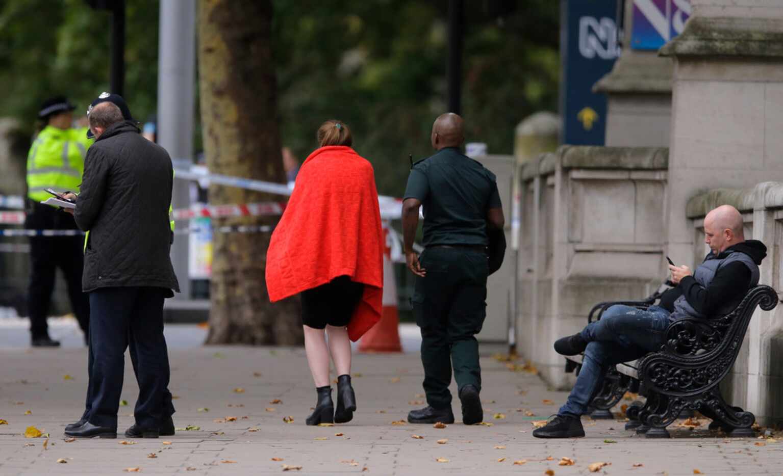 An injured woman wearing a red blanket escorted by a paramedic at the scene of an incident...