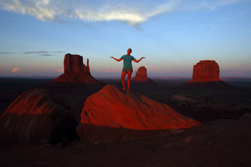 The sun sets over Monument Valley in Arizona while visitors pose for pictures on the red rocks.