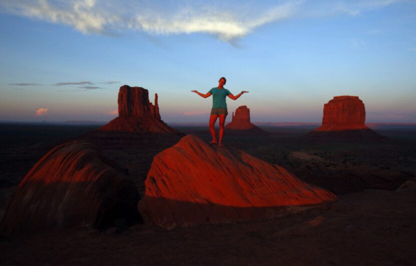 The sun sets over Monument Valley in Arizona while visitors pose for pictures on the red rocks.