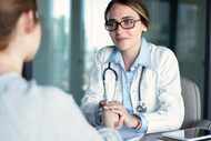 A young female doctor speaks to a patient with back to camera while holding her hand.