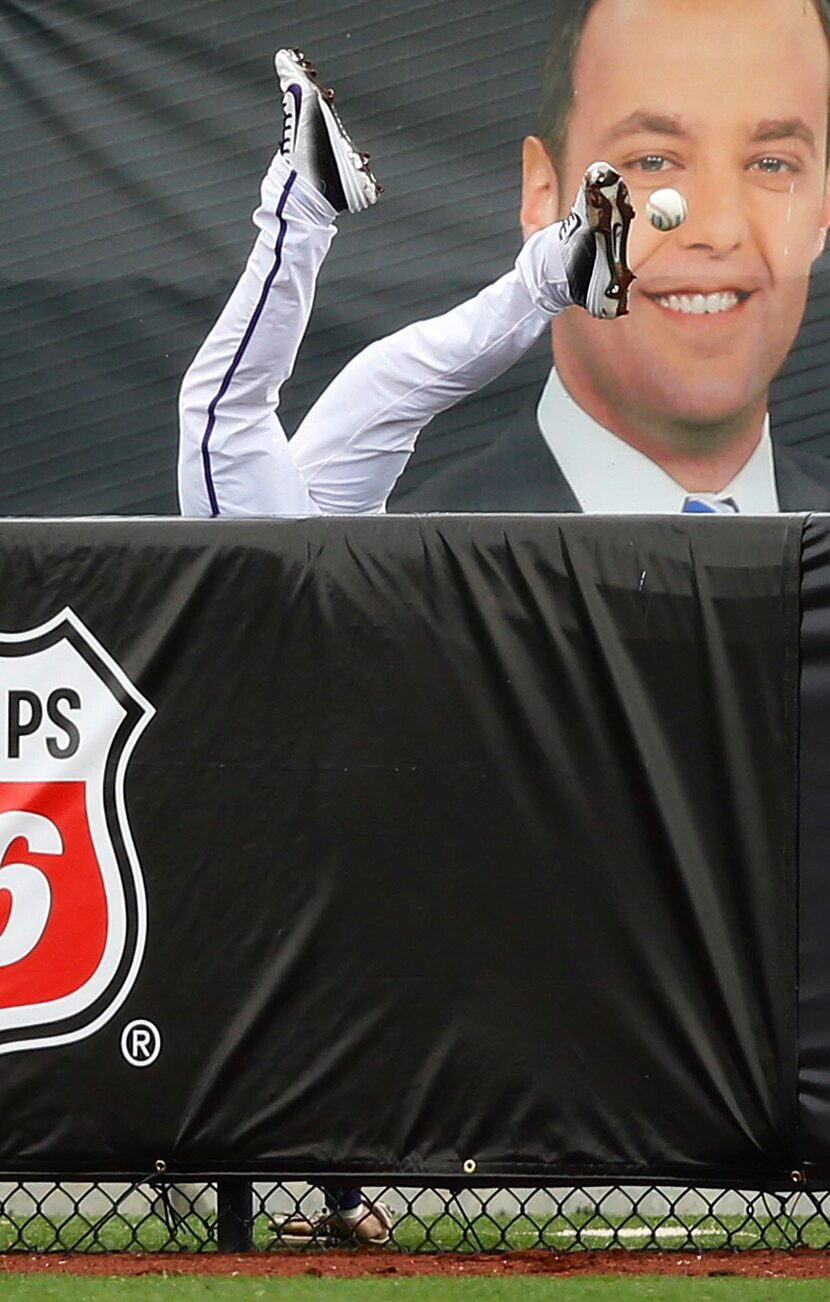  TCU right fielder Nolan Brown tumbles over the outfield fence after attempting a catch on a...