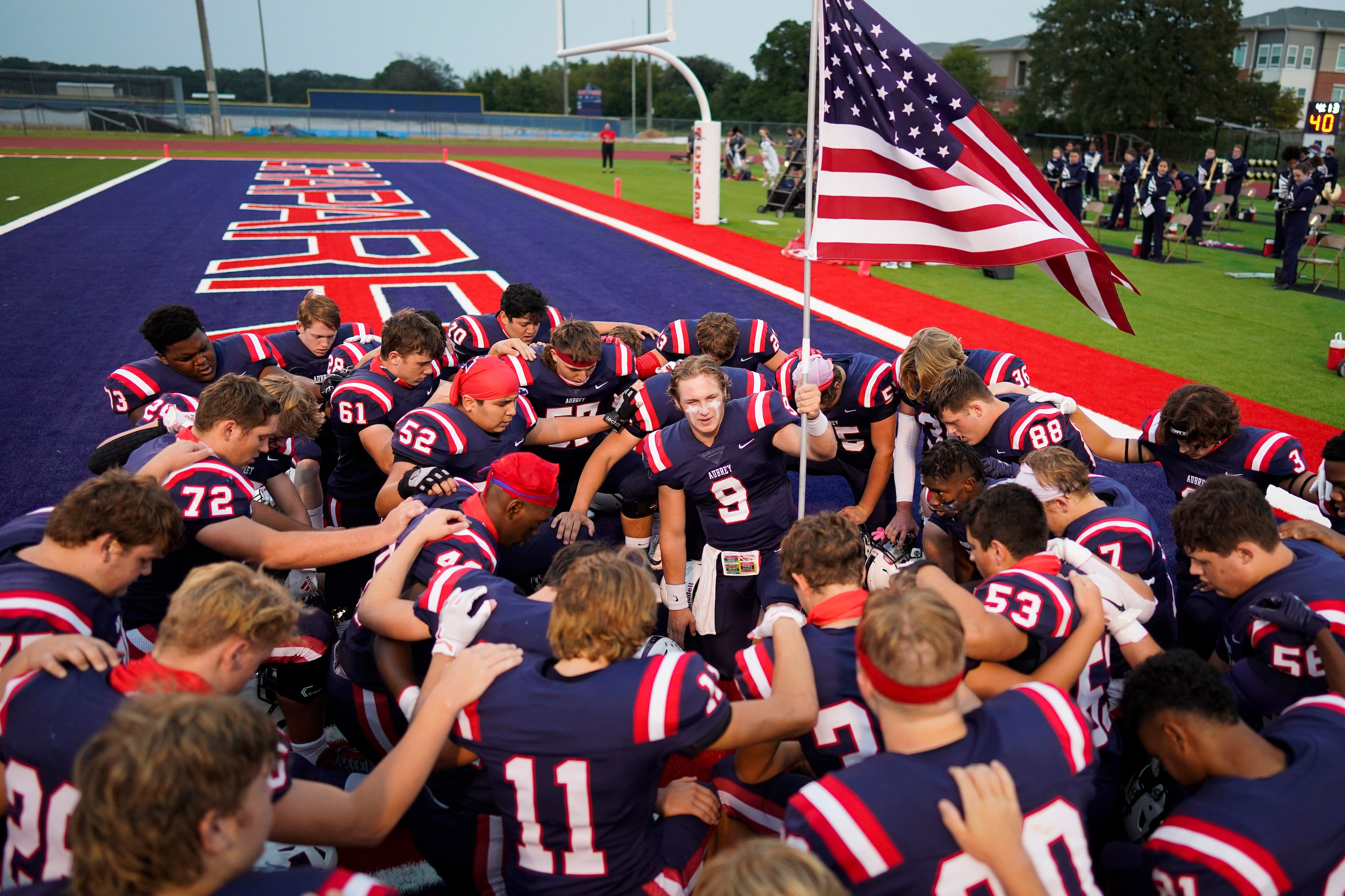 Aubrey quarterback Jaxon Holder holds the American flag as he huddles with his teammates ...