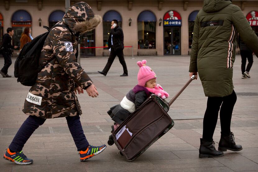 A child rides on a suitcase outside of the Beijing Railway Station.