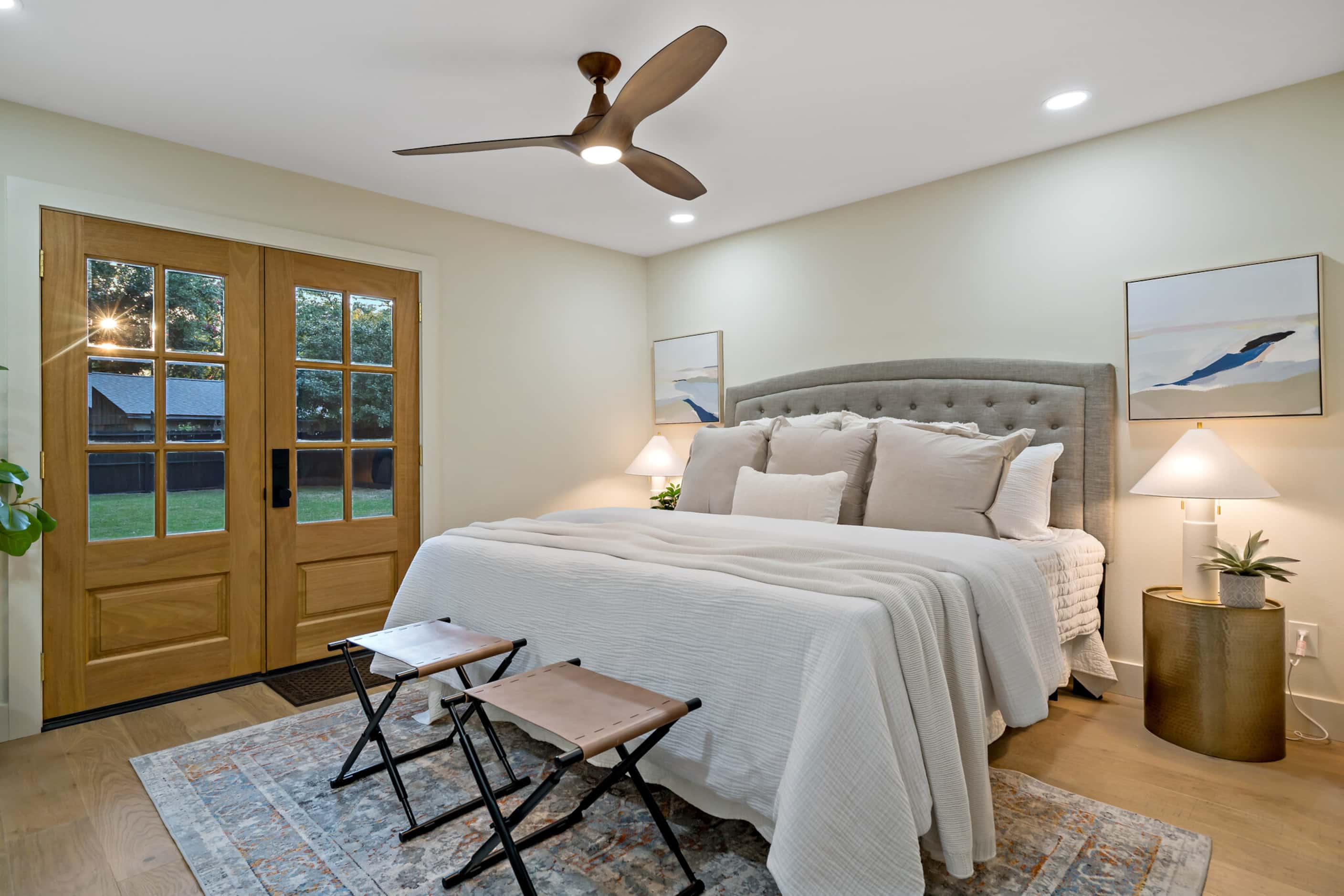 Bedroom with large bed, door to backyard patio, folding stools at end of bed