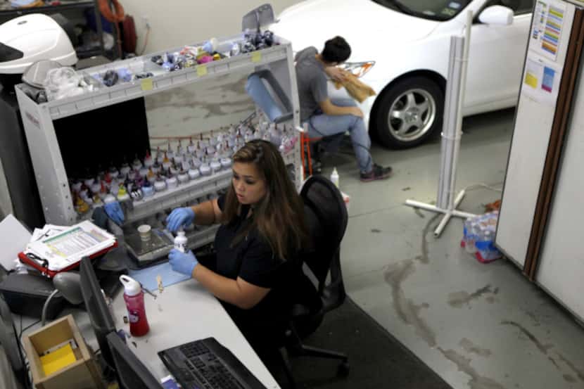 Thy Dam mixes paint at her desk while Dani Webb works on a car. The Colors on Parade...