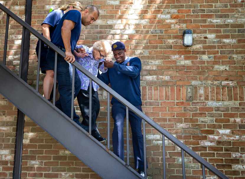 Dallas firefighters help Agnes "Mickey" Santillo, 99, down the stairs at her condominium for...