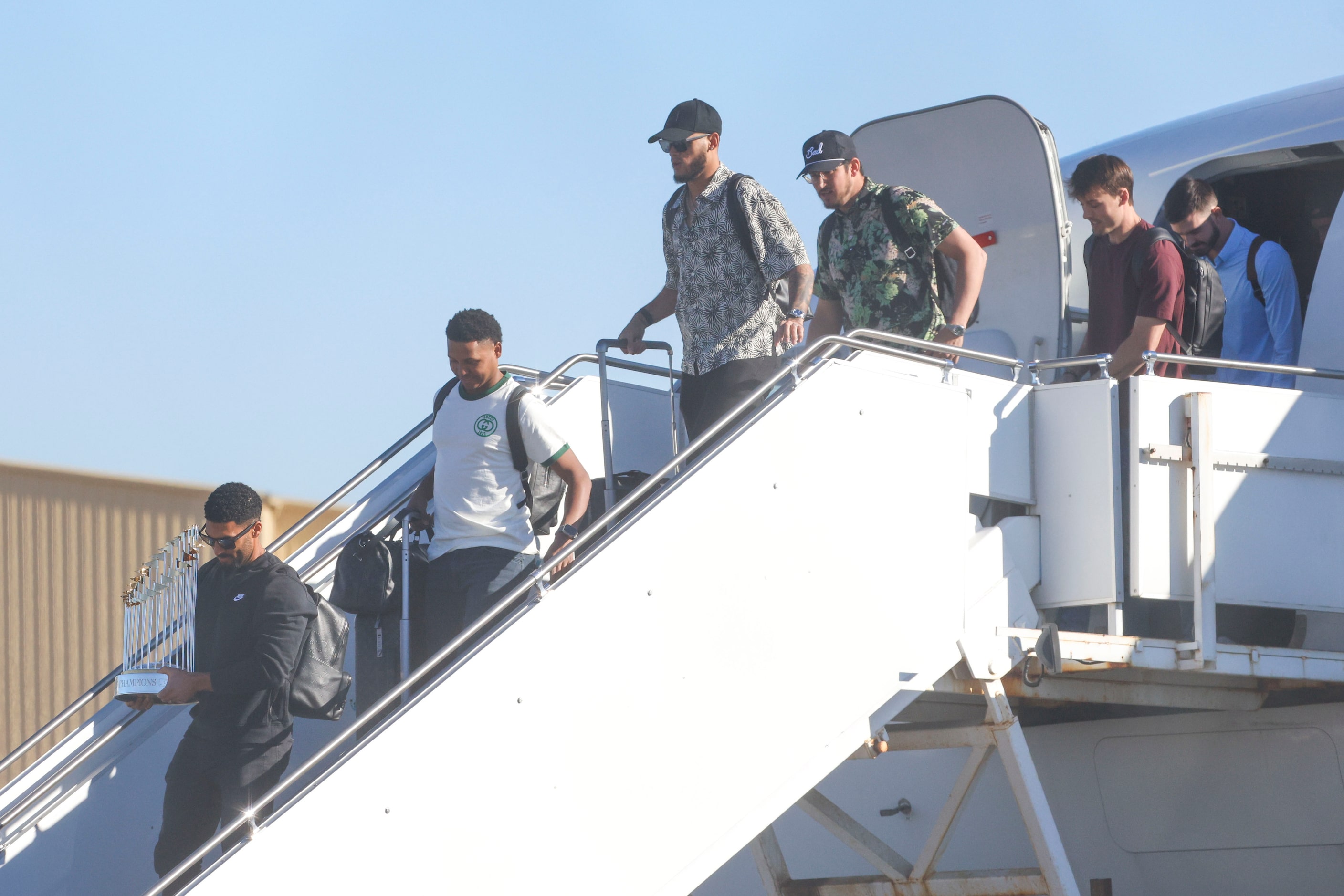 Texas Rangers’ Marcus Semien (left) carrying the commissioner's trophy leads the players...