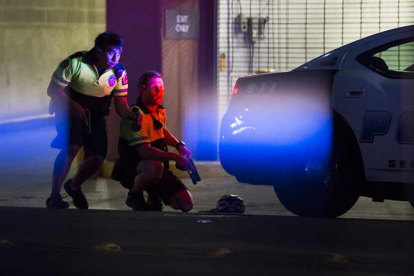 Dallas Police officers take cover behind a vehicle on Lamar Street after shots were fired...