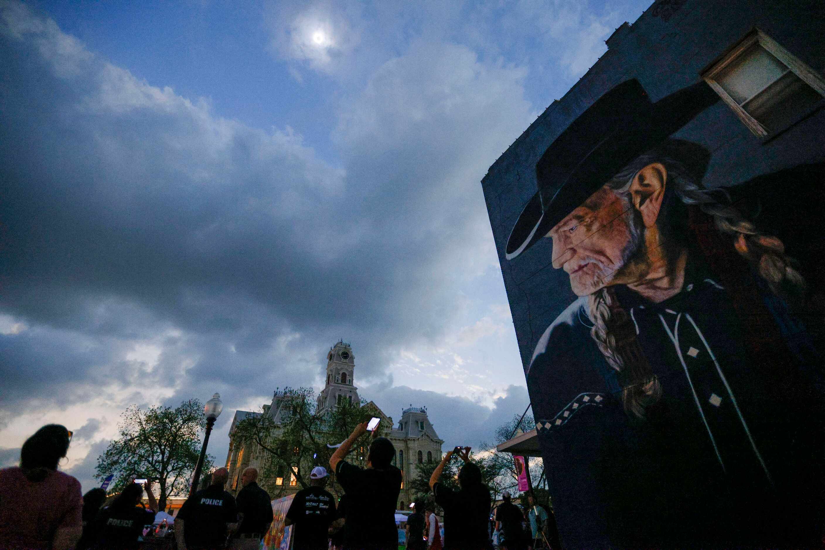 People watch a total solar eclipse over the Hill County Courthouse and a mural of Willie...