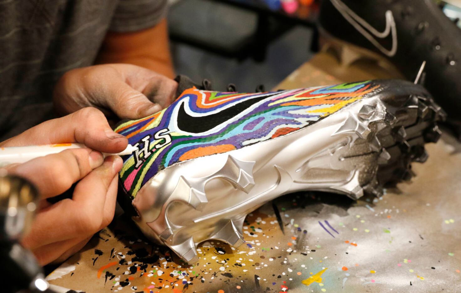 Luke Savage, 16, applies white paint on the HS logo on cleats he created for SportsDayHS in...