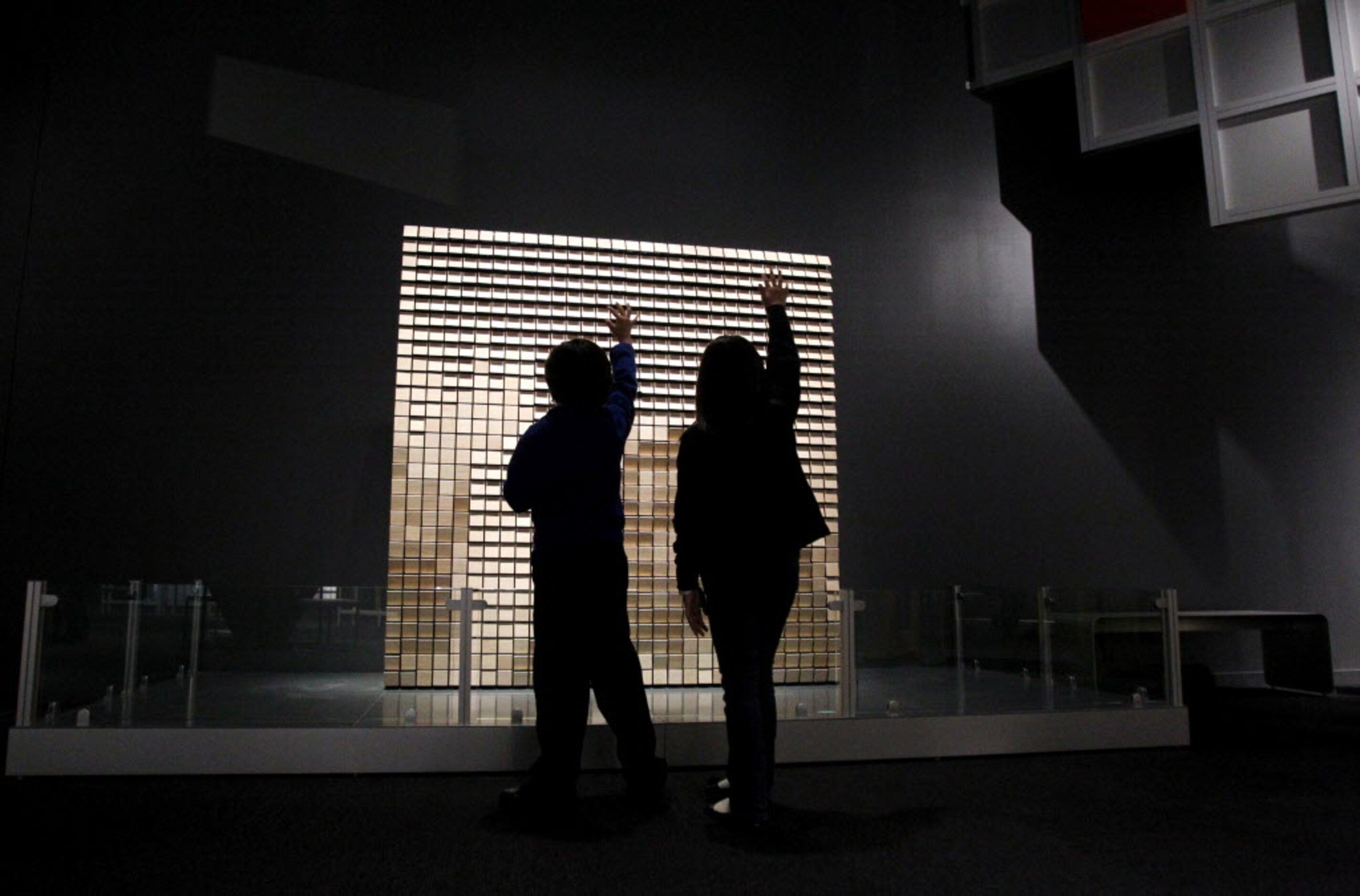 Small wood panels reflect the movements of two visitors at the Perot Museum of Nature and...