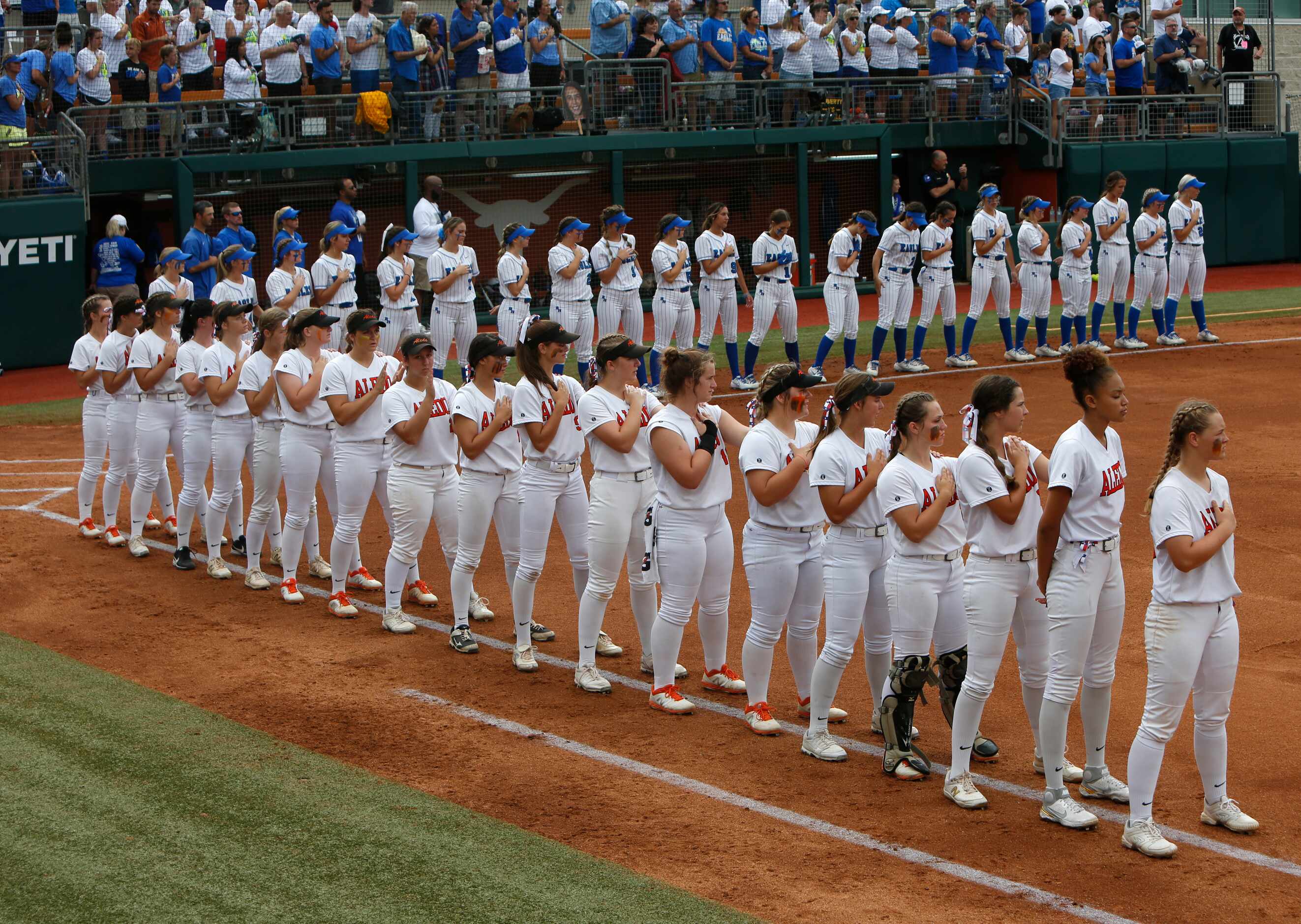 Aledo players (foreground) and Barbers Hill players pause for the playing of the national...