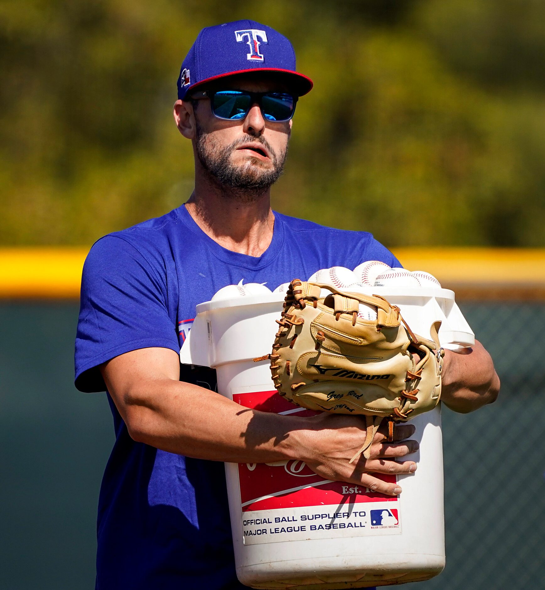 Texas Rangers infielder Greg Bird carries a bucket of baseball from infield practice during...