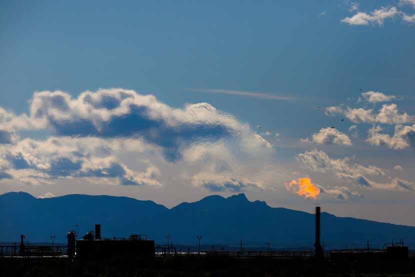 Mountains tower in the background as flames shoot from the flare stack of an oil production...
