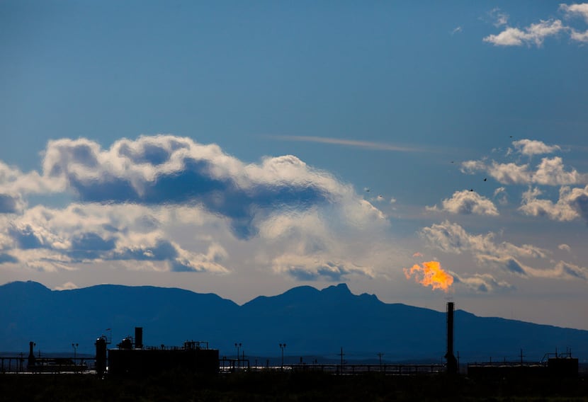 Mountains tower in the background as flames shoot from the flare stack of an oil production...