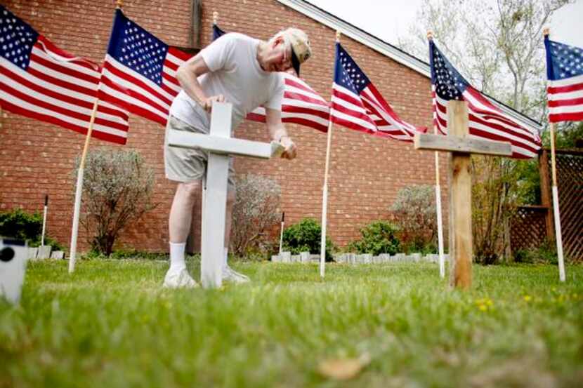 
Bob Gordon paints a cross placed in front of 16 American flags as he helps build a memorial...