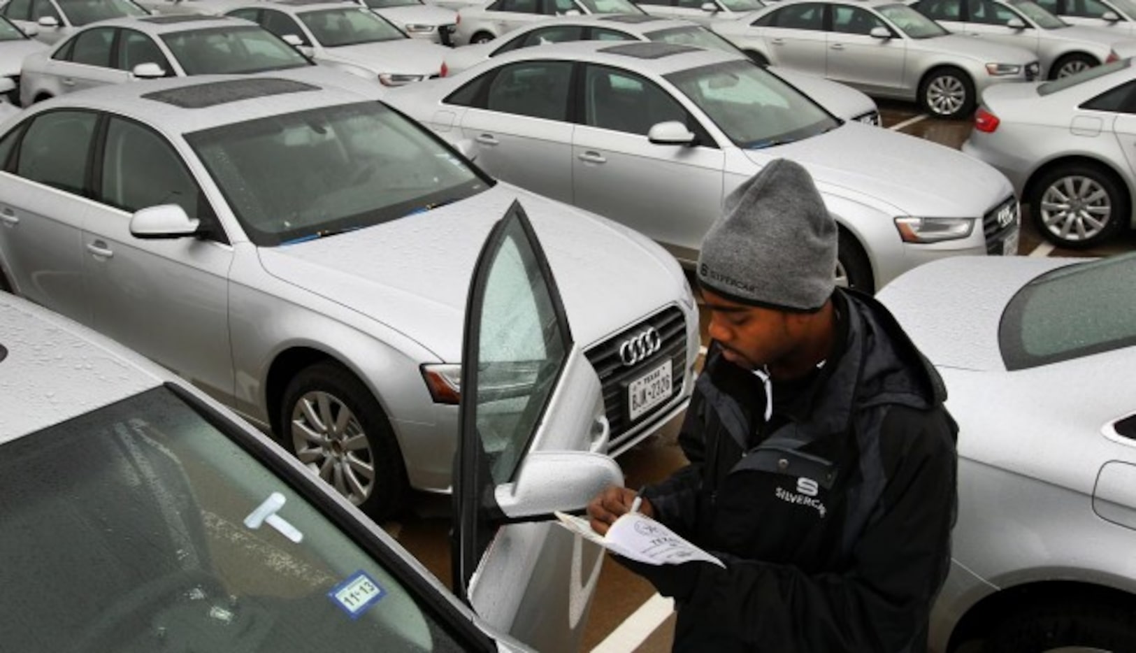 Un empleado de una agencia de renta de vehículos inspecciona un auto recién entregado....