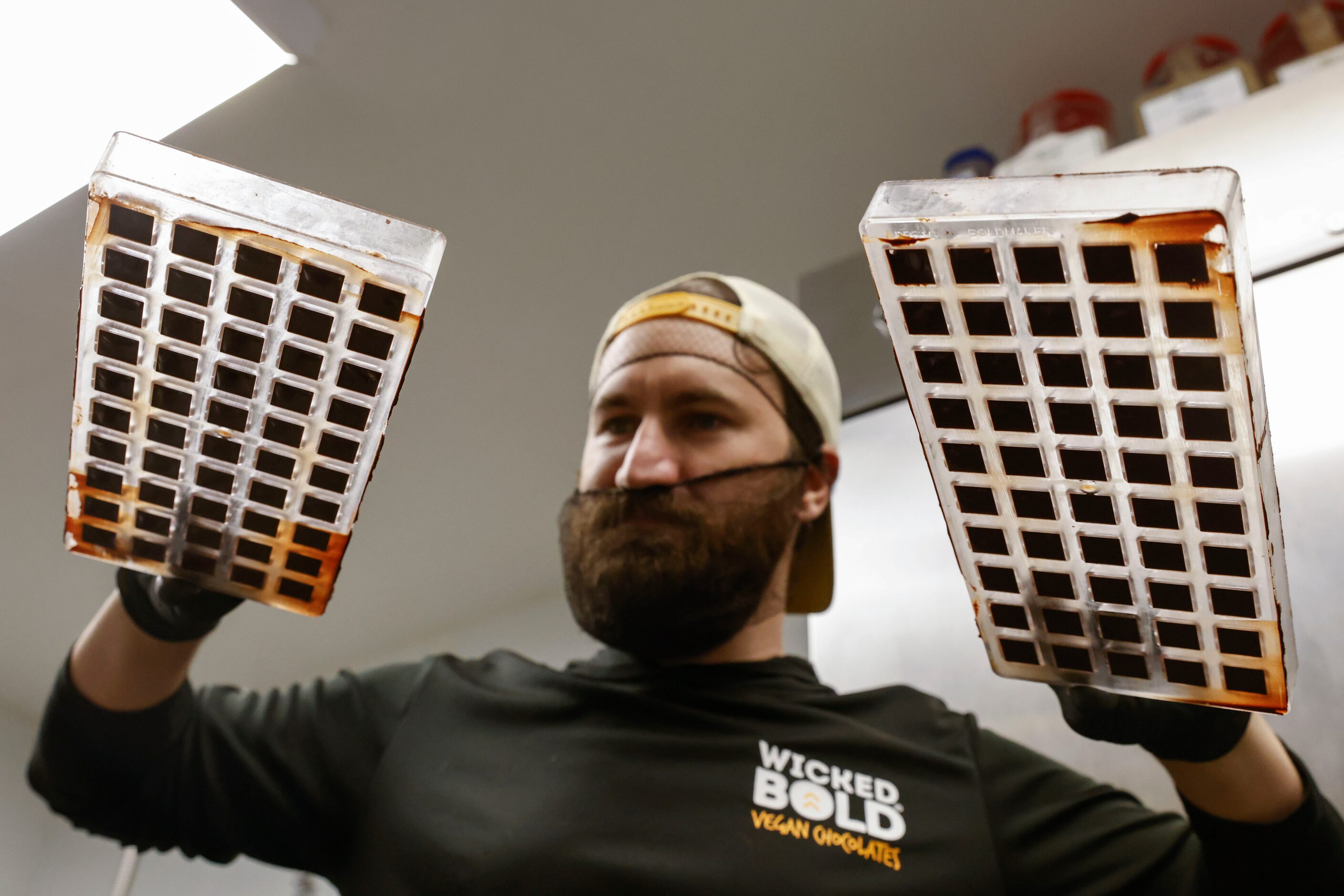 Deric Cahill holds trays of set chocolate ready to be popped out. Next, he bangs the trays...