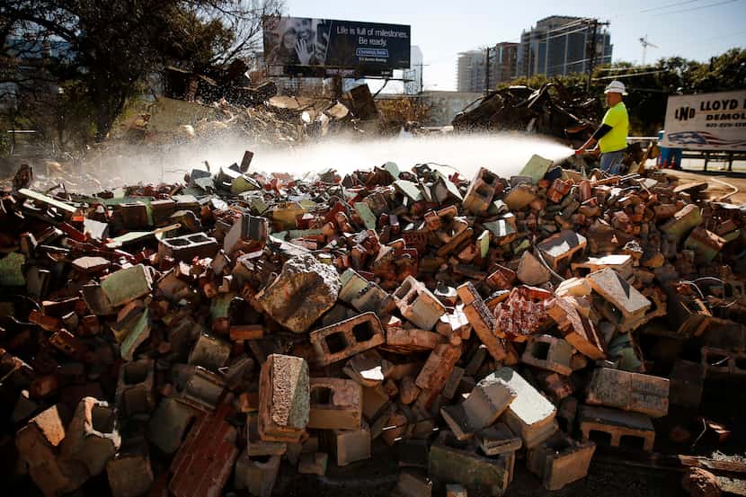 Demolition crewman Alex Robledo sprays water onto a pile of bricks that, until Tuesday, was...