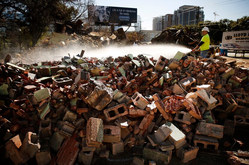 Demolition crewman Alex Robledo sprays water onto a pile of bricks that, until Tuesday, was...