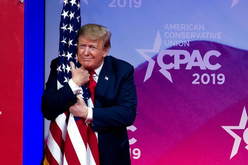 President Donald Trump hugs the American flag as he arrives on stage to speak at the...