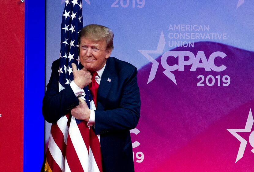 President Donald Trump hugs the American flag as he arrives on stage to speak at the...