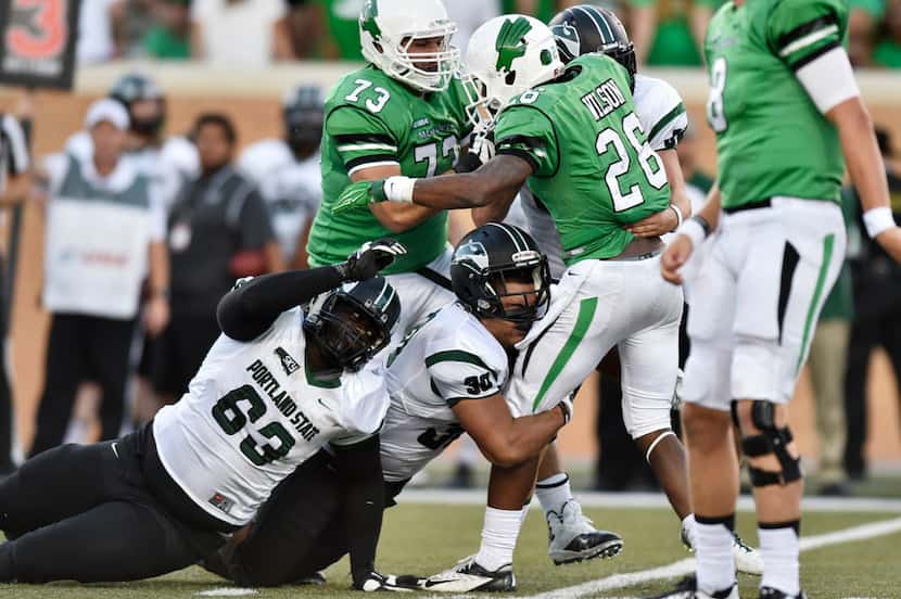 North Texas sophomore running back Jeffrey Wilson (26) stays upright as he's tackled by...