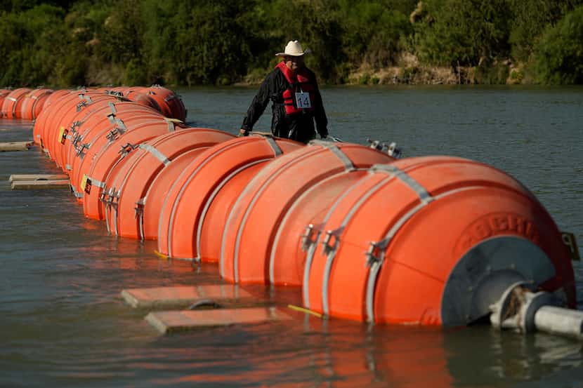 A kayaker walks past large buoys being used as a floating border barrier on the Rio Grande...