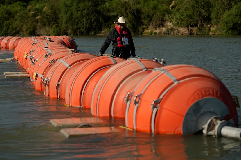 A kayaker walks past large buoys being used as a floating border barrier on the Rio Grande...