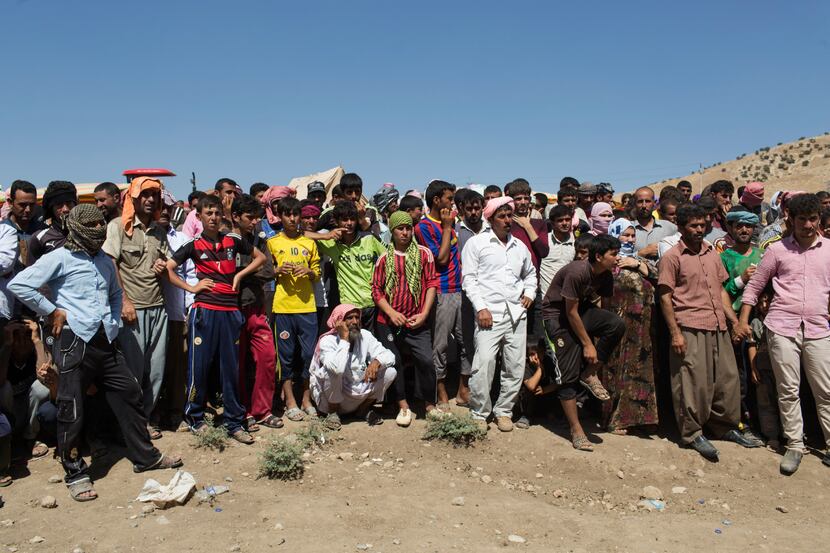 Iraqi Yazidi people wait to receive aid at a makeshift roadside camp near the border...