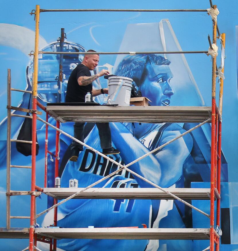 Artist Josh Mittag works on the mural on one of the outside walls of the Dallas Mavericks'...