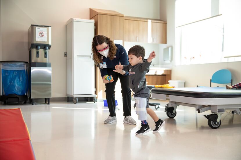 A specialist wearing a mask at Scottish Rite for Children helps a child with a prothesis...