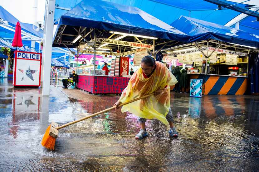 State Fair of Texas employee Mary Muniz uses a broom to move puddles of rain water closer to...