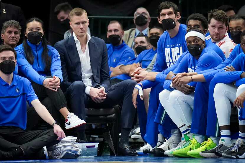 Dallas Mavericks center Kristaps Porzingis (in street clothes at left) watches from the...