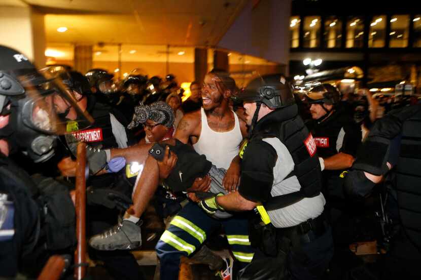 Police and protesters carry a seriously wounded protester into the parking area of the the...