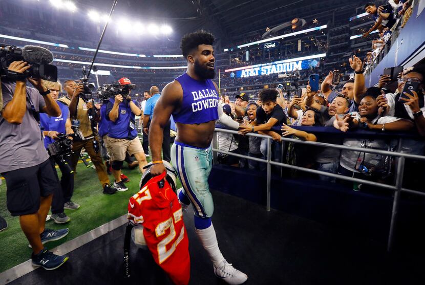 Dallas Cowboys running back Ezekiel Elliott (21) slaps hands with fans as he exits the field...