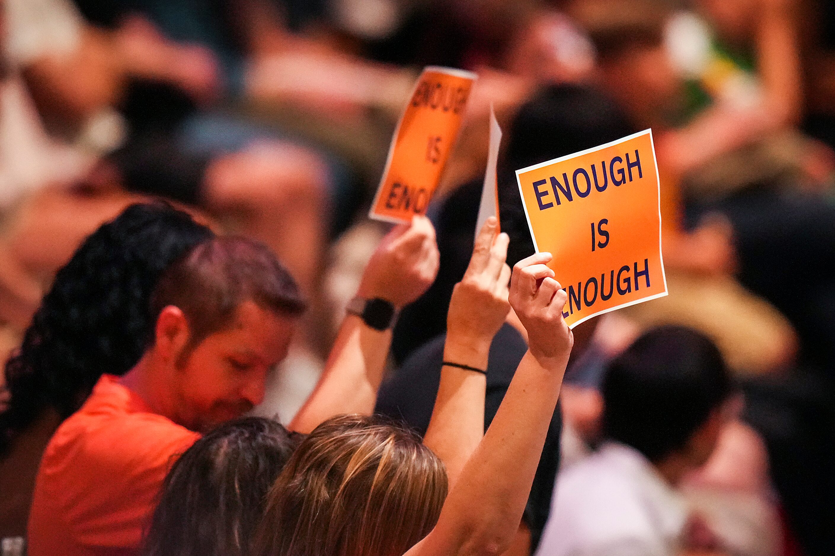 A small group holds up signs reading “Enough is Enough” during a vigil at Cottonwood Creek...