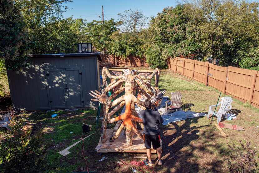 Artist Giovanni Valderas adds glue to a giant skeleton sculpture in his back yard in Dallas...