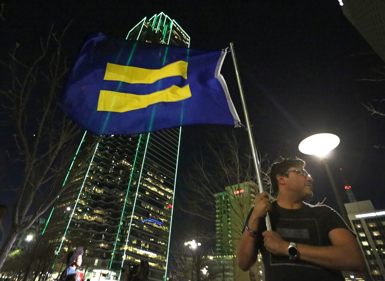 Samuel Sanchez holds a flag with an equality symbol in the evening breeze as protesters...